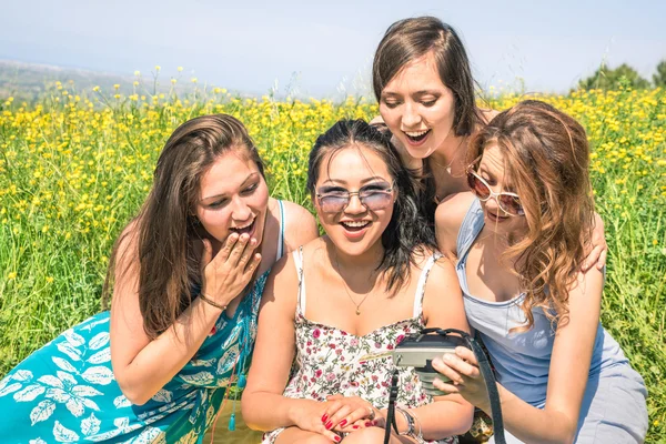 Multiracial girlfriends at countryside picnic watching photos in snapshot instant digital camera - Happy friendship fun concept with young people and new technology trend - Sunny afternoon color tone