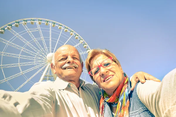 Happy retired senior couple taking selfie at travel around the world - Concept of active playful elderly with mobile phone - Mature people fun lifestyle in sunny day with strong sunlight color tones
