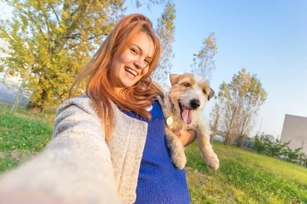 Young redhead woman taking selfie outdoors with cute dog - Concept of friendship and love with people and animals together - Sunny winter afternoon with warm color tones - Tilted horizon composition