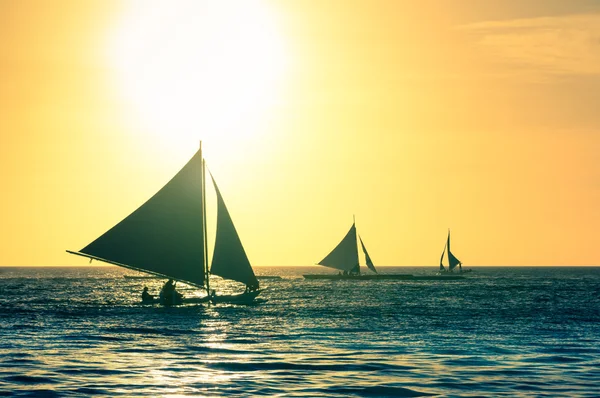 Silhouette of typical sailing boats at sunset in Boracay island - Exclusive travel destination in Philippines - Warm vintage filtered look