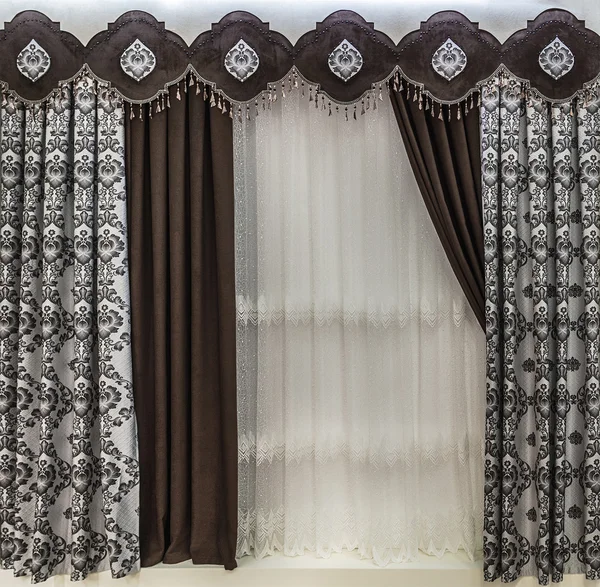 The stylish design of the window opening. Combined brown curtains, a pelmet and a tulle.