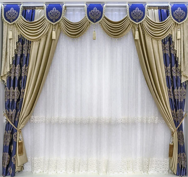 The luxurious design of the windows and walls. Draperies, pelmet and a tulle. The combination of gold-tone curtains and the blue cloth with ornaments.
