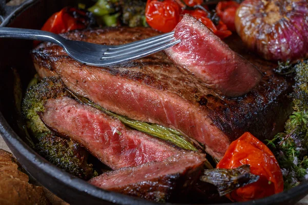 Beef steak medium rare pieces with a garnish of vegetables in a cast iron skillet. meat shot in low key. fatty foods rich in protein. ready meat dish in rustic style