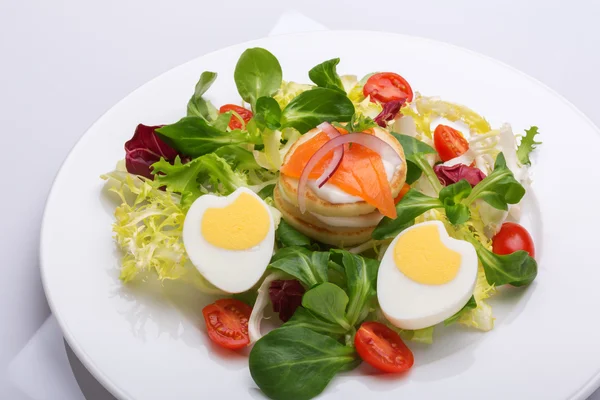 Green salad with eggs in the shape of a heart, salmon, cherry tomatoes