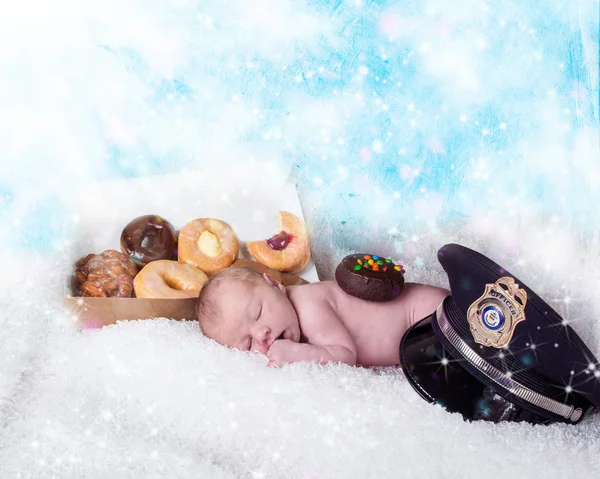 Baby sleeping next to a box of donuts next to a police hat