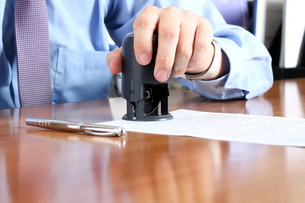 Close-up Of Businessman Hand Pressing a  Stamp On Document in the office