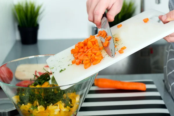 Food, family, cooking and people concept - Man chopping a carrot on cutting board with knife in kitchen