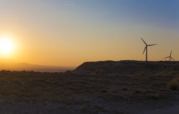 Electric wind turbines farm with sunset light on arid landscape