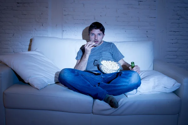 Man sitting at home sofa in living room watching movie or sport in tv eating popcorn and drinking beer
