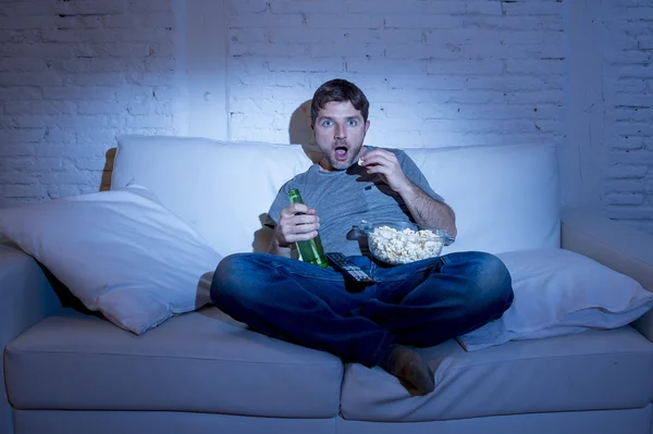Man sitting at home sofa in living room watching movie or sport in tv eating popcorn and drinking beer