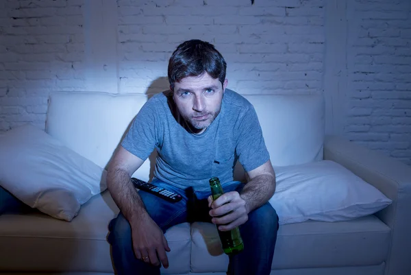 Man at home lying on couch at living room watching sport match on tv drinking beer