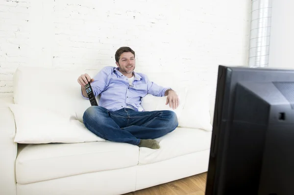 Young happy man watching television smiling and laughing in sofa
