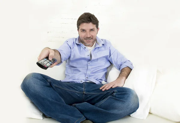 Young happy man watching tv sitting at home living room sofa looking relaxed enjoying television