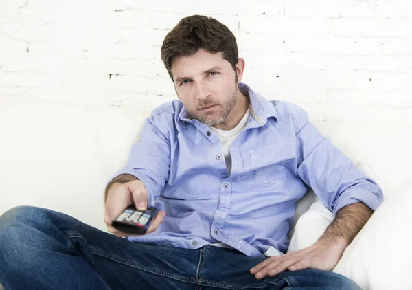 Man watching television lying at home living room sofa with remote control looking very interested