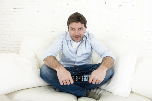 Young happy man watching tv sitting at home living room sofa looking relaxed enjoying television