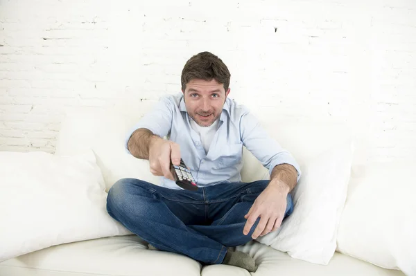 Young happy man watching tv sitting at home living room sofa looking relaxed enjoying television