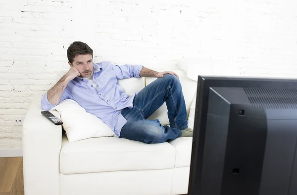 Young happy man watching tv lying at home living room sofal looking relaxed enjoying television