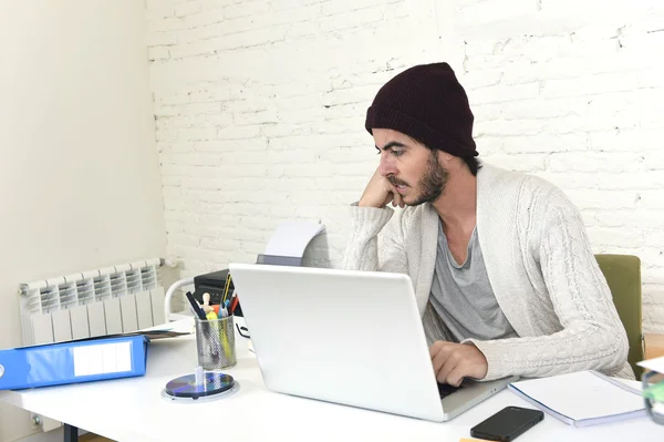 Trendy businessman in cool hipster beanie looking to laptop computer monitor analyzing project