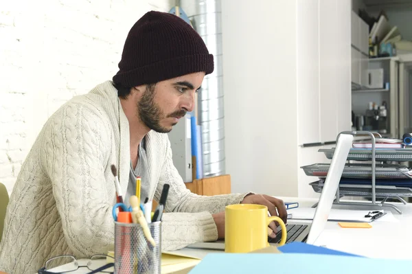 Trendy businessman in cool hipster beanie with coffee working busy at modern home office with compute