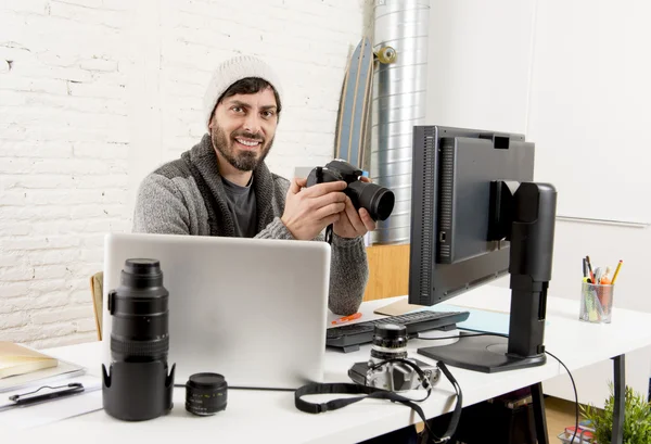 Young attractive press photographer holding photographic camera viewing his work on editor office desk