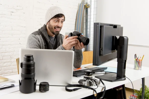 Young attractive press photographer holding photographic camera viewing his work on editor office desk