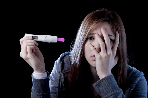 Young woman scared and shocked holding pregnancy test positive result looking unhappy