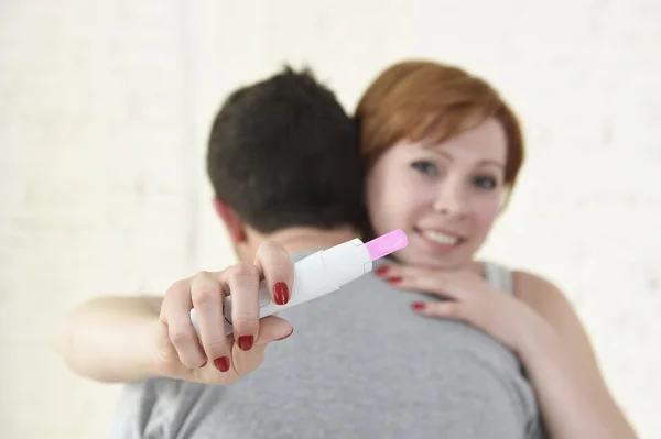 Young happy woman hugging husband holding positive result pregnancy test expecting a baby