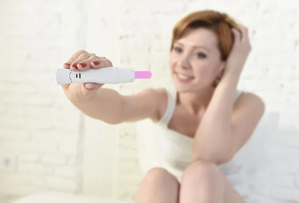 Young attractive pregnant woman holding happy positive result pregnancy test sitting on bed