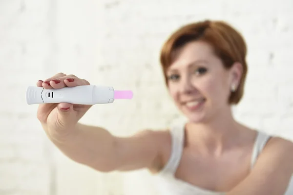 Young attractive pregnant woman holding happy positive result pregnancy test sitting on bed