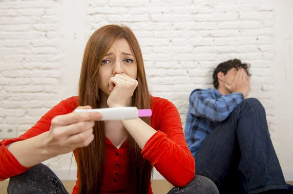Young sad couple scared in shock and surprise reading pink positive pregnancy test overwhelmed in panic