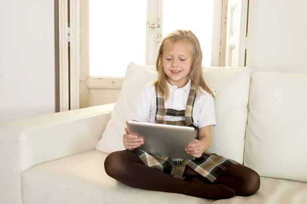 Sweet little girl sitting on home sofa couch using internet app on digital tablet pad
