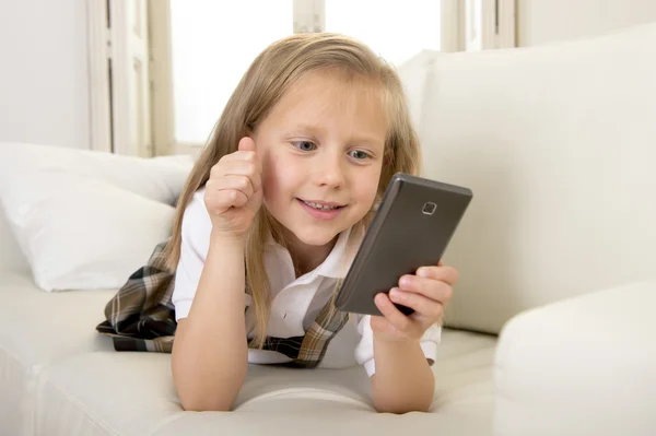 Female child with blond hair sitting on couch using internet app on mobile phone