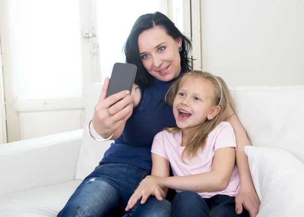 Young happy woman with her little cute blond daughter taking selfie photo with mobile phone