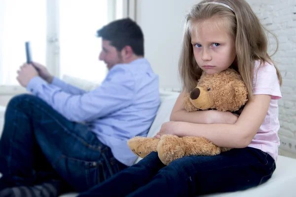 Internet addict father using mobile phone ignoring little sad daughter bored hugging teddy bear