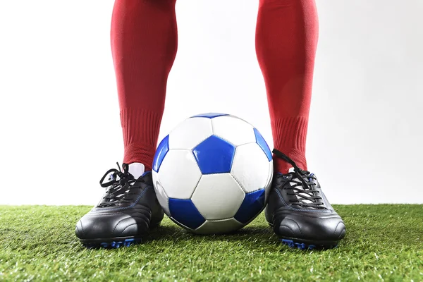 Legs feet of football player in red socks and black shoes posing with the ball playing on green grass pitch