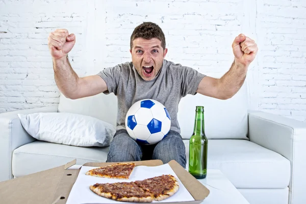 Young man holding ball watching football game on tv at home couch with pizza and beer celebrating crazy goal or victory