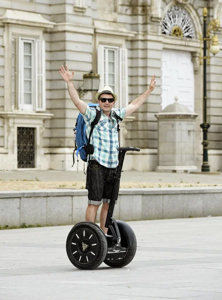 Young happy tourist man with backpack riding city tour segway driving happy and excited visiting Madrid palace
