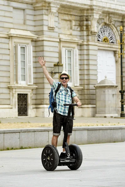 Young happy tourist man with backpack riding city tour segway driving happy and excited visiting Madrid palace