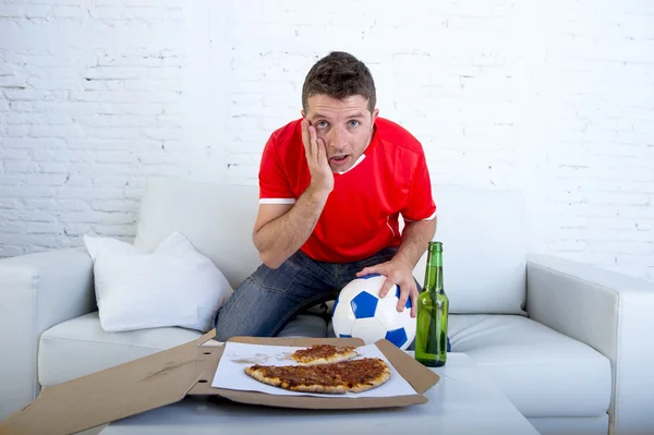Man alone holding ball with beer and pizza in stress wearing team jersey watching football game on tv