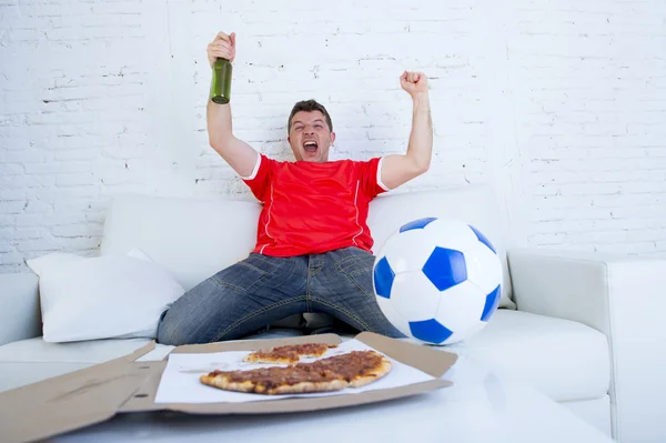 Young football fan man watching game on tv in team jersey celebrating goal crazy happy on couch