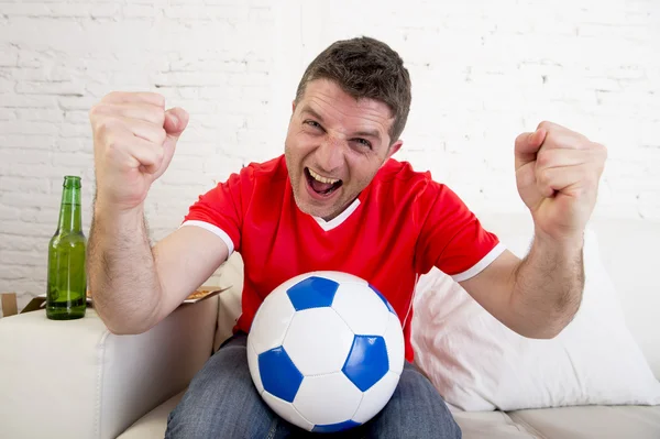 Man watching football on tv wearing team jersey celebrating goal happy on sofa