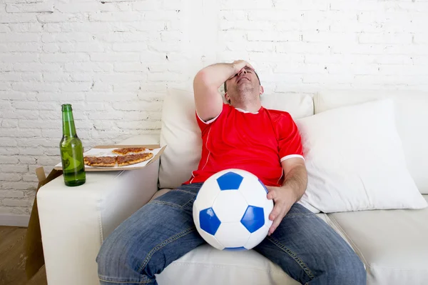 Soccer fan watching football game on TV sad disappointed leaning on couch hopeless