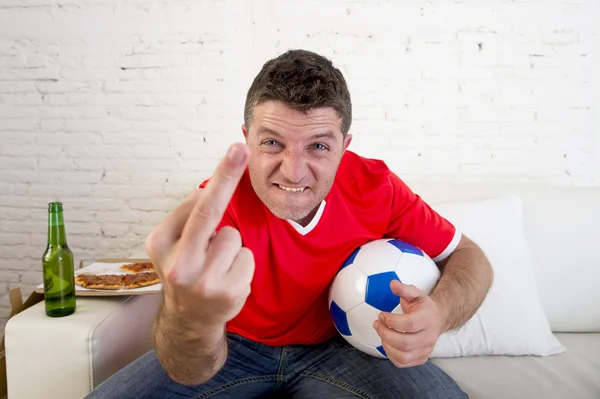 Young man holding ball watching football game on tv gesturing upset and crazy angry giving the finger