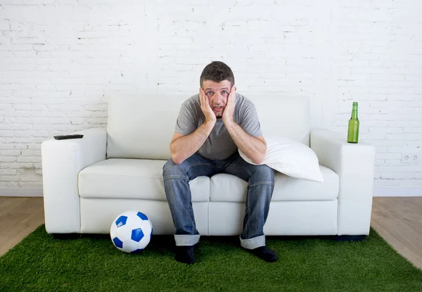Football fan watching tv match on sofa with grass pitch carpet i