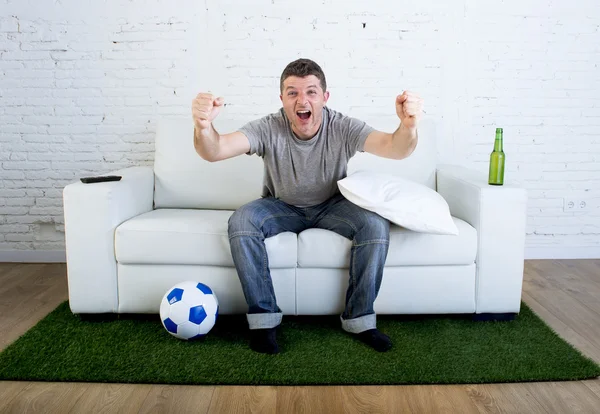 Football fan watching tv match on sofa with grass pitch carpet celebrating goal