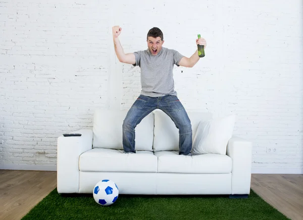 Football fan watching tv match on sofa with grass pitch carpet celebrating goal