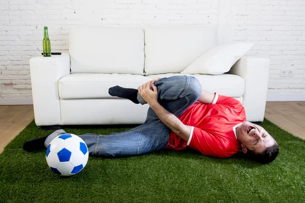 Fanatic football fan on green grass carpet emulating soccer stadium pitch mocking player in pain hurt on ankle