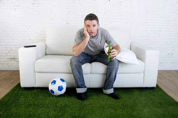 Football fan watching tv match on sofa with grass pitch carpet i