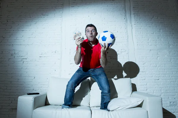 Crazy man holding money and soccer ball watching football on tv internet online bet gambling