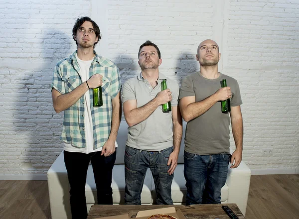 Friends standing in front of television emulating football players listening to team national anthem